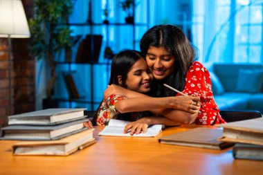 Hintli abla çalışma masasında evde otururken kalemle küçük kız kardeşine ders veriyor. Asyalı küçük kızlar ev ortamında ev ödevi yaparken birlikte öğrenme ve çalışma üzerine odaklandılar.