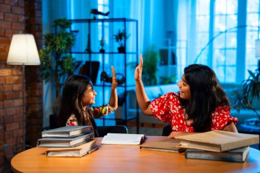 Hintli abla çalışma masasında evde otururken kalemle küçük kız kardeşine ders veriyor. Asyalı küçük kızlar ev ortamında ev ödevi yaparken birlikte öğrenme ve çalışma üzerine odaklandılar.