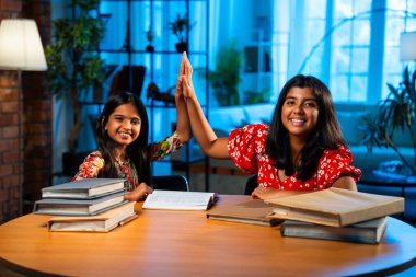 Hintli abla çalışma masasında evde otururken kalemle küçük kız kardeşine ders veriyor. Asyalı küçük kızlar ev ortamında ev ödevi yaparken birlikte öğrenme ve çalışma üzerine odaklandılar.