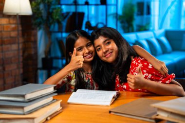 Hintli abla çalışma masasında evde otururken kalemle küçük kız kardeşine ders veriyor. Asyalı küçük kızlar ev ortamında ev ödevi yaparken birlikte öğrenme ve çalışma üzerine odaklandılar.