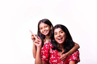 Beyaz arka planda dururken kameraya sarılıp gülümseyen Hintli küçük kardeş kızlar. Renkli elbiseler içinde Asyalı küçük kız kardeşler neşeli ifadelerle sevgi ve neşe gösteriyorlar.