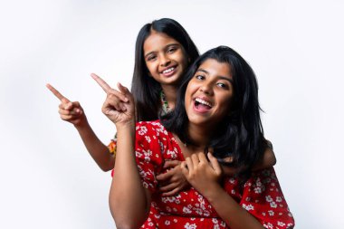 Hintli küçük kız kardeşler beyaz arka plana karşı boş alanı işaret ediyor, Asyalı küçük kardeşler fotokopi alanında el kol geziyor, neşeli ifadeler ve eğlenceli iletişim konsepti gösteren izole edilmiş stüdyo görüntüleri.