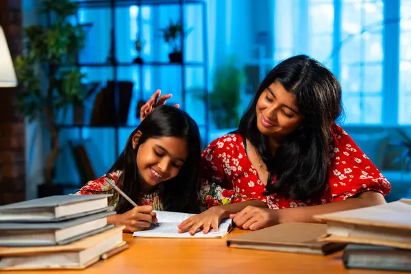 Hintli abla çalışma masasında evde otururken kalemle küçük kız kardeşine ders veriyor. Asyalı küçük kızlar ev ortamında ev ödevi yaparken birlikte öğrenme ve çalışma üzerine odaklandılar.
