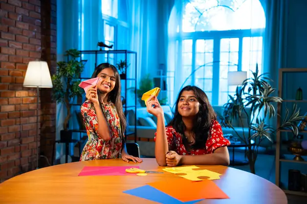 Hintli kardeş kardeşler içeride birlikte otururken makas kullanarak kağıt işi yapıyorlar. Küçük Asyalı kızlar rahat ev ortamında eğlenceli DIY etkinliği sırasında odak yaratıcılığıyla renkli çarşaf kesiyorlar.