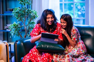 Hintli küçük kız kardeşler tablet bilgisayarda komik videolar izlerken evde oturuyorlar, Asyalı kız kardeşler dijital eğlencenin, çocukluk eğlencesinin, mutluluğun, aile bağlarının tadını çıkarıyorlar.