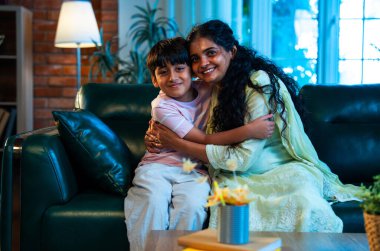 Hintli anne küçük çocuk, modern evde kanepenin üzerinde sarılıp öpüşüyor, birlikte iyi vakit geçiriyorlar, sevgi, sevgi, sıcaklık, ilgi, mutluluk, aile içi çocuk ilişkileri tarzı.