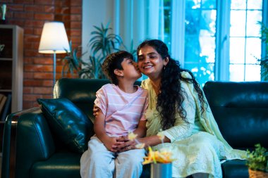 Hintli anne küçük çocuk, modern evde kanepenin üzerinde sarılıp öpüşüyor, birlikte iyi vakit geçiriyorlar, sevgi, sevgi, sıcaklık, ilgi, mutluluk, aile içi çocuk ilişkileri tarzı.