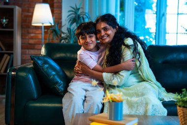 Hintli anne küçük çocuk, modern evde kanepenin üzerinde sarılıp öpüşüyor, birlikte iyi vakit geçiriyorlar, sevgi, sevgi, sıcaklık, ilgi, mutluluk, aile içi çocuk ilişkileri tarzı.