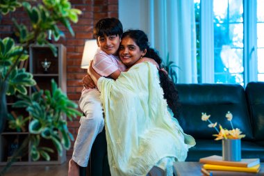 Hintli anne küçük çocuk, modern evde kanepenin üzerinde sarılıp öpüşüyor, birlikte iyi vakit geçiriyorlar, sevgi, sevgi, sıcaklık, ilgi, mutluluk, aile içi çocuk ilişkileri tarzı.