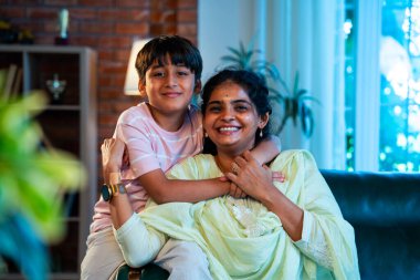 Hintli anne küçük çocuk kanepenin üzerinde modern evde sarılıyor, birlikte iyi vakit geçiriyorlar, sevgi ve sıcaklık gösteriyorlar, ebeveyn-çocuk ilişkisi yaşam tarzı aile mutluluğu kavramı.