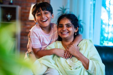 Hintli anne küçük çocuk kanepenin üzerinde modern evde sarılıyor, birlikte iyi vakit geçiriyorlar, sevgi ve sıcaklık gösteriyorlar, ebeveyn-çocuk ilişkisi yaşam tarzı aile mutluluğu kavramı.