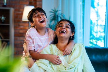 Hintli anne küçük çocuk kanepenin üzerinde modern evde sarılıyor, birlikte iyi vakit geçiriyorlar, sevgi ve sıcaklık gösteriyorlar, ebeveyn-çocuk ilişkisi yaşam tarzı aile mutluluğu kavramı.