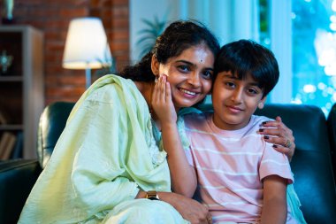 Hintli anne küçük çocuk kanepenin üzerinde modern evde sarılıyor, birlikte iyi vakit geçiriyorlar, sevgi ve sıcaklık gösteriyorlar, ebeveyn-çocuk ilişkisi yaşam tarzı aile mutluluğu kavramı.