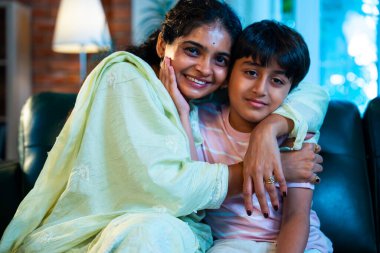 Hintli anne küçük çocuk kanepenin üzerinde modern evde sarılıyor, birlikte iyi vakit geçiriyorlar, sevgi ve sıcaklık gösteriyorlar, ebeveyn-çocuk ilişkisi yaşam tarzı aile mutluluğu kavramı.