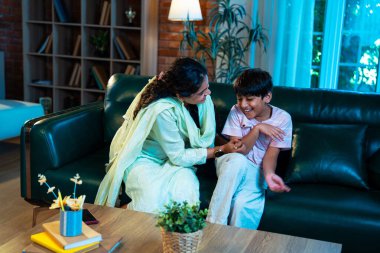 Hintli çocuk ve anne gülerek modern evde kanepede oturuyorlar, birlikte kaliteli zaman geçiriyorlar, şefkat gösteriyorlar, sevgi, neşe, mutluluk, ebeveyn-çocuk ilişkisi yaşam tarzı kapalı