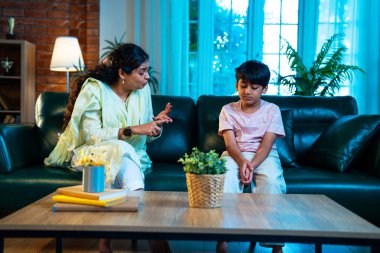 Hintli anne oğlunu azarlıyor, modern evde koltukta otururken, iyi alışkanlıklar öğretiyor, disiplini teşvik ediyor, kaliteli zaman geçirtiyor, çocuğa sevgiyle yol gösteriyor, ebeveyn çocuk ilişkisini kapalı alanda gösteriyor.