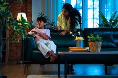 Hintli anne oğlunu azarlıyor, modern evde koltukta otururken, iyi alışkanlıklar öğretiyor, disiplini teşvik ediyor, kaliteli zaman geçirtiyor, çocuğa sevgiyle yol gösteriyor, ebeveyn çocuk ilişkisini kapalı alanda gösteriyor.