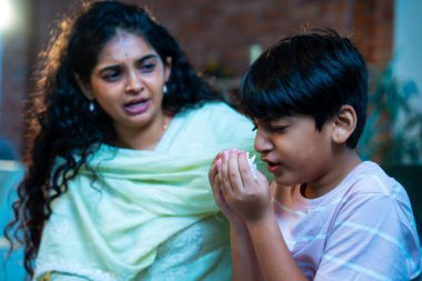 Hintli küçük bir çocuk modern bir evde annesinin yanında otururken öksürüyor, viral semptomlar gösteriyor, kendini iyi hissetmiyor, annesinin bakımı, çocuk bakımı, aile bağı, sağlık farkındalığı, bakımı,