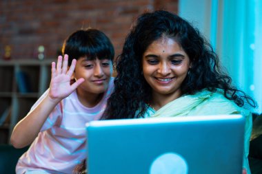 Hintli küçük çocuk ve anne internette sörf yapıyor ya da internetten alışveriş yapıyor modern evdeki kanepede otururken, birlikte kaliteli zaman geçiriyorlar, bağlanma, bağ kurma, ebeveyn çocuk yaşam tarzı gösteriyorlar.