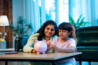 Hintli anne oğul, modern evdeki domuz kumbarasına bozuk para koyuyor, küçük yaşta para biriktirmeyi öğretiyor, kaliteli bağ kurma zamanını paylaşıyor, ebeveyn öğrenimi, şefkat, rehberlik...