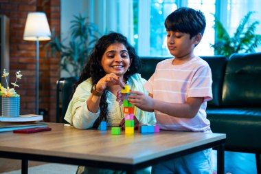 Hintli anne oğul modern evde tahta oyuncak blok kulesi yapıyor, birlikte kaliteli oyun zamanı geçiriyor, yaratıcılık inşa ediyor, eğlenceyi, neşeyi, bağı, ebeveyn çocuk etkileşimini, aile yaşam tarzını evde paylaşıyor.