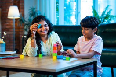 Hintli anne oğul modern evde tahta oyuncak blok kulesi yapıyor, birlikte kaliteli oyun zamanı geçiriyor, yaratıcılık inşa ediyor, eğlenceyi, neşeyi, bağı, ebeveyn çocuk etkileşimini, aile yaşam tarzını evde paylaşıyor.