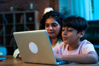 Hintli evlat dizüstü bilgisayar kullanmayı öğrenirken, anne merakla modern evde izliyor, birlikte kaliteli zaman geçiriyorlar, teknolojiyi keşfediyorlar, neşeyi paylaşıyorlar, ebeveyn bağı kuruyorlar, öğrenmeyi büyütüyorlar.