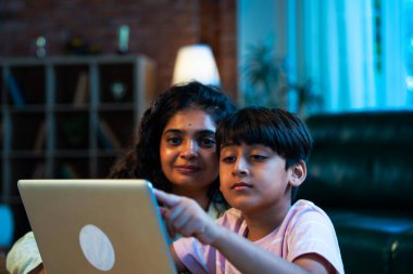 Hintli evlat dizüstü bilgisayar kullanmayı öğrenirken, anne merakla modern evde izliyor, birlikte kaliteli zaman geçiriyorlar, teknolojiyi keşfediyorlar, neşeyi paylaşıyorlar, ebeveyn bağı kuruyorlar, öğrenmeyi büyütüyorlar.