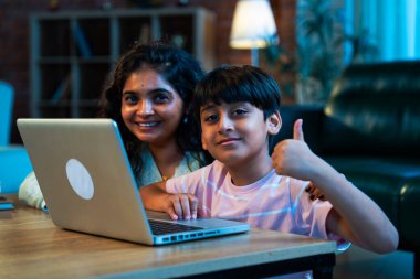 Hintli evlat dizüstü bilgisayar kullanmayı öğrenirken, anne merakla modern evde izliyor, birlikte kaliteli zaman geçiriyorlar, teknolojiyi keşfediyorlar, neşeyi paylaşıyorlar, ebeveyn bağı kuruyorlar, öğrenmeyi büyütüyorlar.