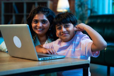 Hintli evlat dizüstü bilgisayar kullanmayı öğrenirken, anne merakla modern evde izliyor, birlikte kaliteli zaman geçiriyorlar, teknolojiyi keşfediyorlar, neşeyi paylaşıyorlar, ebeveyn bağı kuruyorlar, öğrenmeyi büyütüyorlar.