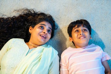 Hintli anne oğul modern evde halıda yatarken konuşuyor, birlikte kaliteli zaman geçiriyorlar, sevgi, neşe, sıcaklık, bağ, ebeveyn çocuk ilişkisi, kapalı alanda aile yaşam tarzı paylaşıyorlar.