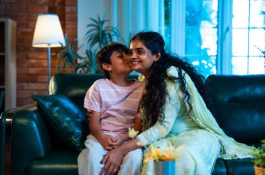 Hintli anne küçük çocuk, modern evde kanepenin üzerinde sarılıp öpüşüyor, birlikte iyi vakit geçiriyorlar, sevgi, sevgi, sıcaklık, ilgi, mutluluk, aile içi çocuk ilişkileri tarzı.