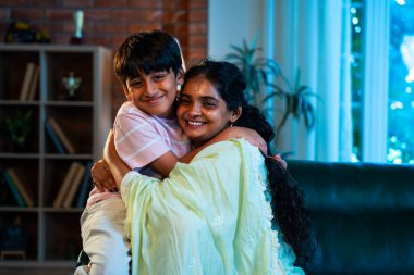 Hintli anne küçük çocuk, modern evde kanepenin üzerinde sarılıp öpüşüyor, birlikte iyi vakit geçiriyorlar, sevgi, sevgi, sıcaklık, ilgi, mutluluk, aile içi çocuk ilişkileri tarzı.