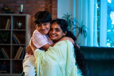 Hintli anne küçük çocuk, modern evde kanepenin üzerinde sarılıp öpüşüyor, birlikte iyi vakit geçiriyorlar, sevgi, sevgi, sıcaklık, ilgi, mutluluk, aile içi çocuk ilişkileri tarzı.