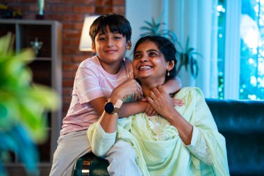 Hintli anne küçük çocuk kanepenin üzerinde modern evde sarılıyor, birlikte iyi vakit geçiriyorlar, sevgi ve sıcaklık gösteriyorlar, ebeveyn-çocuk ilişkisi yaşam tarzı aile mutluluğu kavramı.