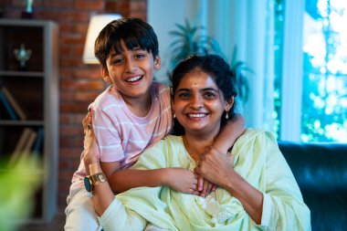 Hintli anne küçük çocuk kanepenin üzerinde modern evde sarılıyor, birlikte iyi vakit geçiriyorlar, sevgi ve sıcaklık gösteriyorlar, ebeveyn-çocuk ilişkisi yaşam tarzı aile mutluluğu kavramı.