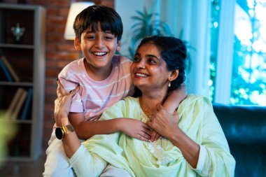 Hintli anne küçük çocuk kanepenin üzerinde modern evde sarılıyor, birlikte iyi vakit geçiriyorlar, sevgi ve sıcaklık gösteriyorlar, ebeveyn-çocuk ilişkisi yaşam tarzı aile mutluluğu kavramı.