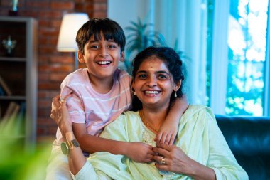 Hintli anne küçük çocuk kanepenin üzerinde modern evde sarılıyor, birlikte iyi vakit geçiriyorlar, sevgi ve sıcaklık gösteriyorlar, ebeveyn-çocuk ilişkisi yaşam tarzı aile mutluluğu kavramı.