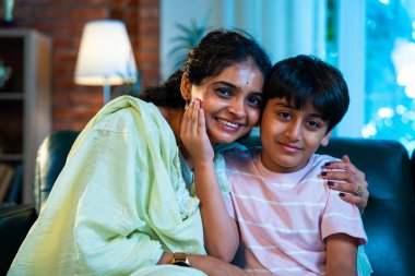 Hintli anne küçük çocuk kanepenin üzerinde modern evde sarılıyor, birlikte iyi vakit geçiriyorlar, sevgi ve sıcaklık gösteriyorlar, ebeveyn-çocuk ilişkisi yaşam tarzı aile mutluluğu kavramı.