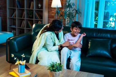 Hintli çocuk ve anne gülerek modern evde kanepede oturuyorlar, birlikte kaliteli zaman geçiriyorlar, şefkat gösteriyorlar, sevgi, neşe, mutluluk, ebeveyn-çocuk ilişkisi yaşam tarzı kapalı