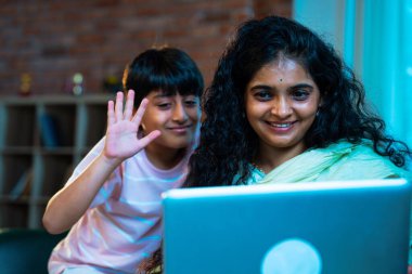 Hintli küçük çocuk ve anne internette sörf yapıyor ya da internetten alışveriş yapıyor modern evdeki kanepede otururken, birlikte kaliteli zaman geçiriyorlar, bağlanma, bağ kurma, ebeveyn çocuk yaşam tarzı gösteriyorlar.