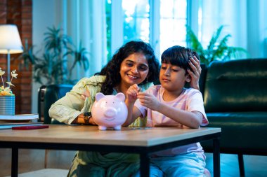 Hintli anne oğul, modern evdeki domuz kumbarasına bozuk para koyuyor, küçük yaşta para biriktirmeyi öğretiyor, kaliteli bağ kurma zamanını paylaşıyor, ebeveyn öğrenimi, şefkat, rehberlik...