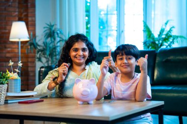 Hintli anne oğul, modern evdeki domuz kumbarasına bozuk para koyuyor, küçük yaşta para biriktirmeyi öğretiyor, kaliteli bağ kurma zamanını paylaşıyor, ebeveyn öğrenimi, şefkat, rehberlik...