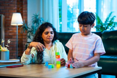 Hintli anne oğul modern evde tahta oyuncak blok kulesi yapıyor, birlikte kaliteli oyun zamanı geçiriyor, yaratıcılık inşa ediyor, eğlenceyi, neşeyi, bağı, ebeveyn çocuk etkileşimini, aile yaşam tarzını evde paylaşıyor.