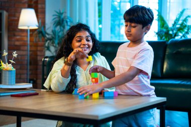 Hintli anne oğul modern evde tahta oyuncak blok kulesi yapıyor, birlikte kaliteli oyun zamanı geçiriyor, yaratıcılık inşa ediyor, eğlenceyi, neşeyi, bağı, ebeveyn çocuk etkileşimini, aile yaşam tarzını evde paylaşıyor.