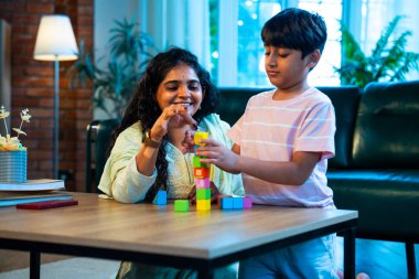 Hintli anne oğul modern evde tahta oyuncak blok kulesi yapıyor, birlikte kaliteli oyun zamanı geçiriyor, yaratıcılık inşa ediyor, eğlenceyi, neşeyi, bağı, ebeveyn çocuk etkileşimini, aile yaşam tarzını evde paylaşıyor.