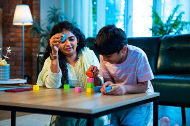 Hintli anne oğul modern evde tahta oyuncak blok kulesi yapıyor, birlikte kaliteli oyun zamanı geçiriyor, yaratıcılık inşa ediyor, eğlenceyi, neşeyi, bağı, ebeveyn çocuk etkileşimini, aile yaşam tarzını evde paylaşıyor.