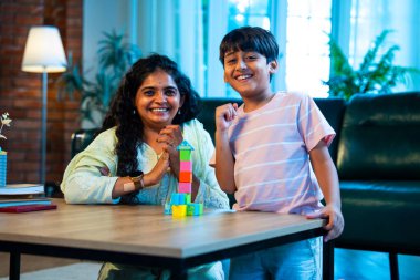 Hintli anne oğul modern evde tahta oyuncak blok kulesi yapıyor, birlikte kaliteli oyun zamanı geçiriyor, yaratıcılık inşa ediyor, eğlenceyi, neşeyi, bağı, ebeveyn çocuk etkileşimini, aile yaşam tarzını evde paylaşıyor.
