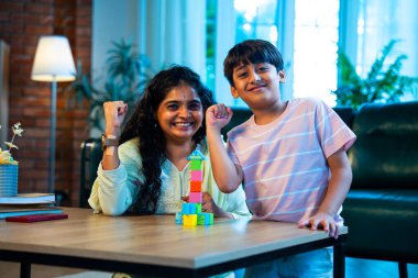 Hintli anne oğul modern evde tahta oyuncak blok kulesi yapıyor, birlikte kaliteli oyun zamanı geçiriyor, yaratıcılık inşa ediyor, eğlenceyi, neşeyi, bağı, ebeveyn çocuk etkileşimini, aile yaşam tarzını evde paylaşıyor.