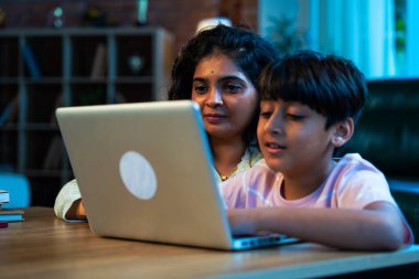 Hintli evlat dizüstü bilgisayar kullanmayı öğrenirken, anne merakla modern evde izliyor, birlikte kaliteli zaman geçiriyorlar, teknolojiyi keşfediyorlar, neşeyi paylaşıyorlar, ebeveyn bağı kuruyorlar, öğrenmeyi büyütüyorlar.